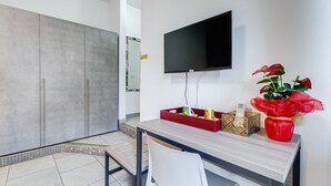 Una camera moderna con una TV a schermo piatto montata a parete, una scrivania in legno con una sedia e un vaso rosso con una pianta.