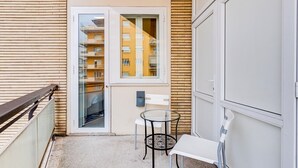 Un balcone con una porta vetrata, un tavolino, due sedie e un armadietto bianco.