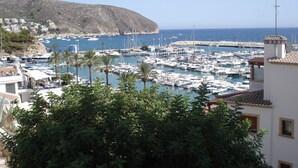 Un port de plaisance avec des bateaux amarrés, une colline en arrière-plan et des bâtiments dotés de balcons donnant sur l’eau.