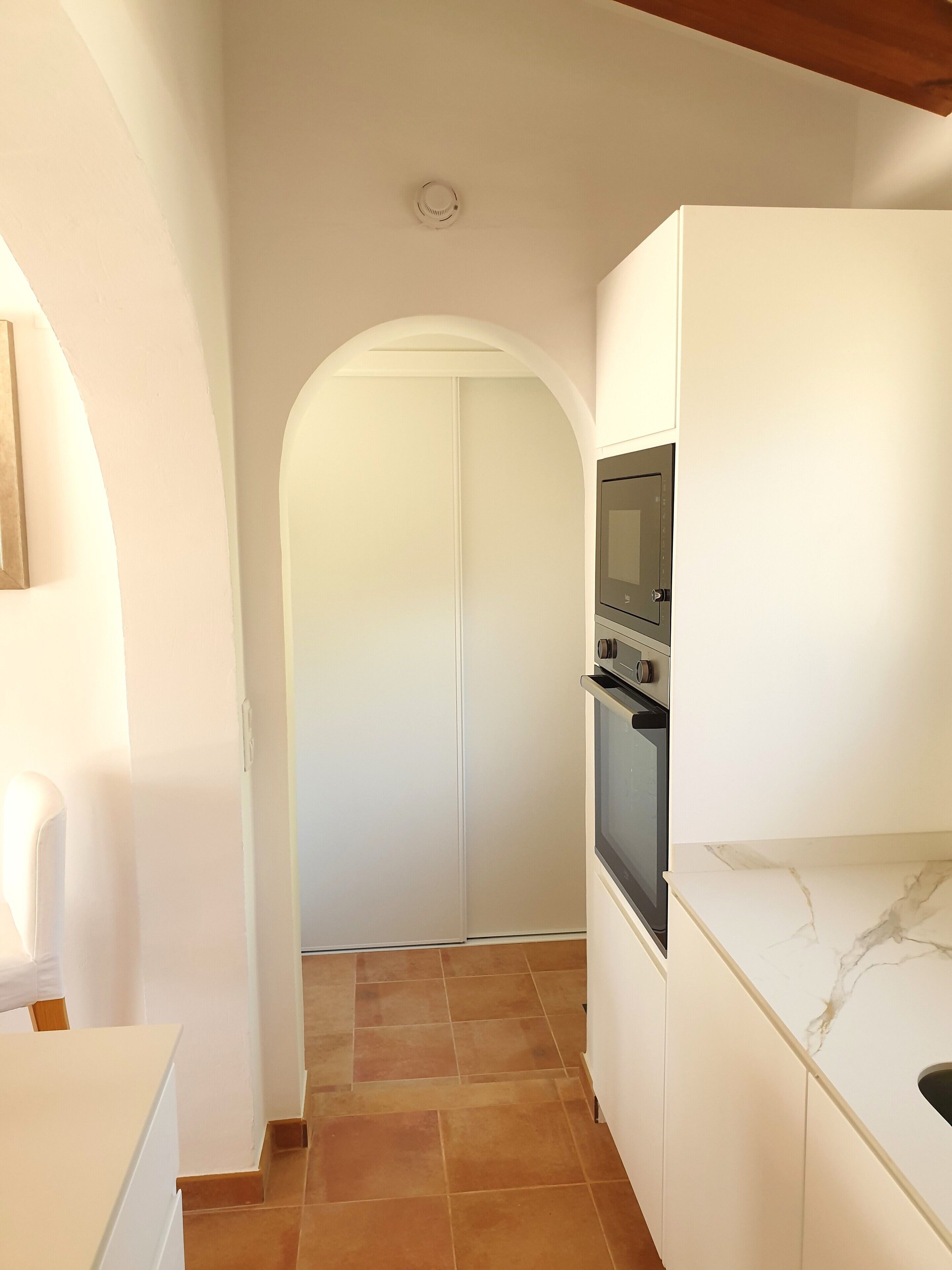 A narrow kitchen with white cabinets, a built-in oven, and a marble countertop.
