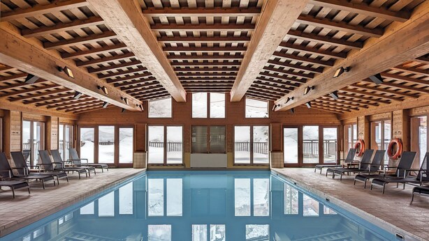 Una piscina interior con vigas de madera y ventanas amplias.