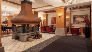 Un hall con una chimenea grande, vigas de madera, asientos de cuero rojo y un candelabro.