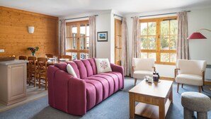 Una sala de estar acogedora con una pared de madera, un sofá rosa, una mesa de centro de madera y una zona de comedor con una mesa y sillas de madera.
