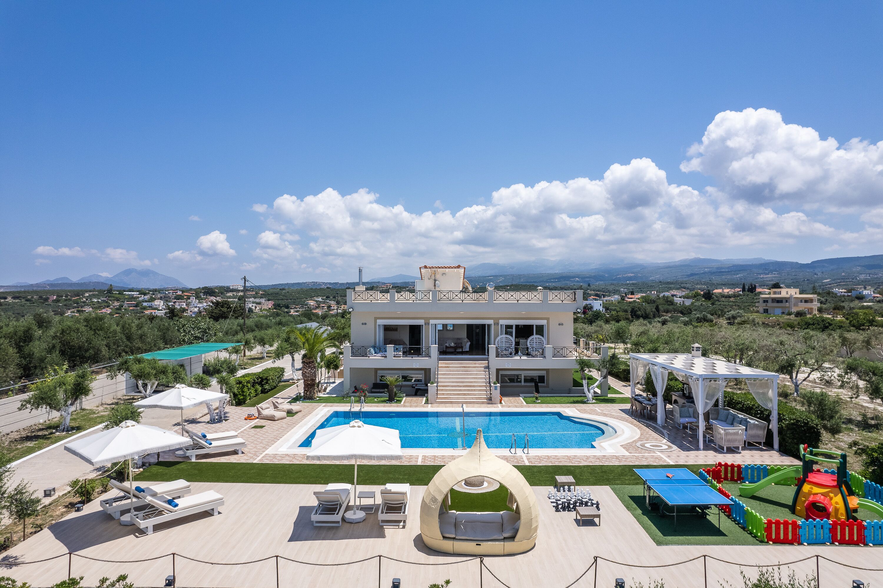 A large, modern villa with a swimming pool, outdoor seating, and a play area.