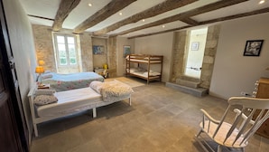 Une chambre rustique avec des poutres apparentes, un lit superposé, un lit simple avec une literie à motifs floraux, une chaise et une petite table.
