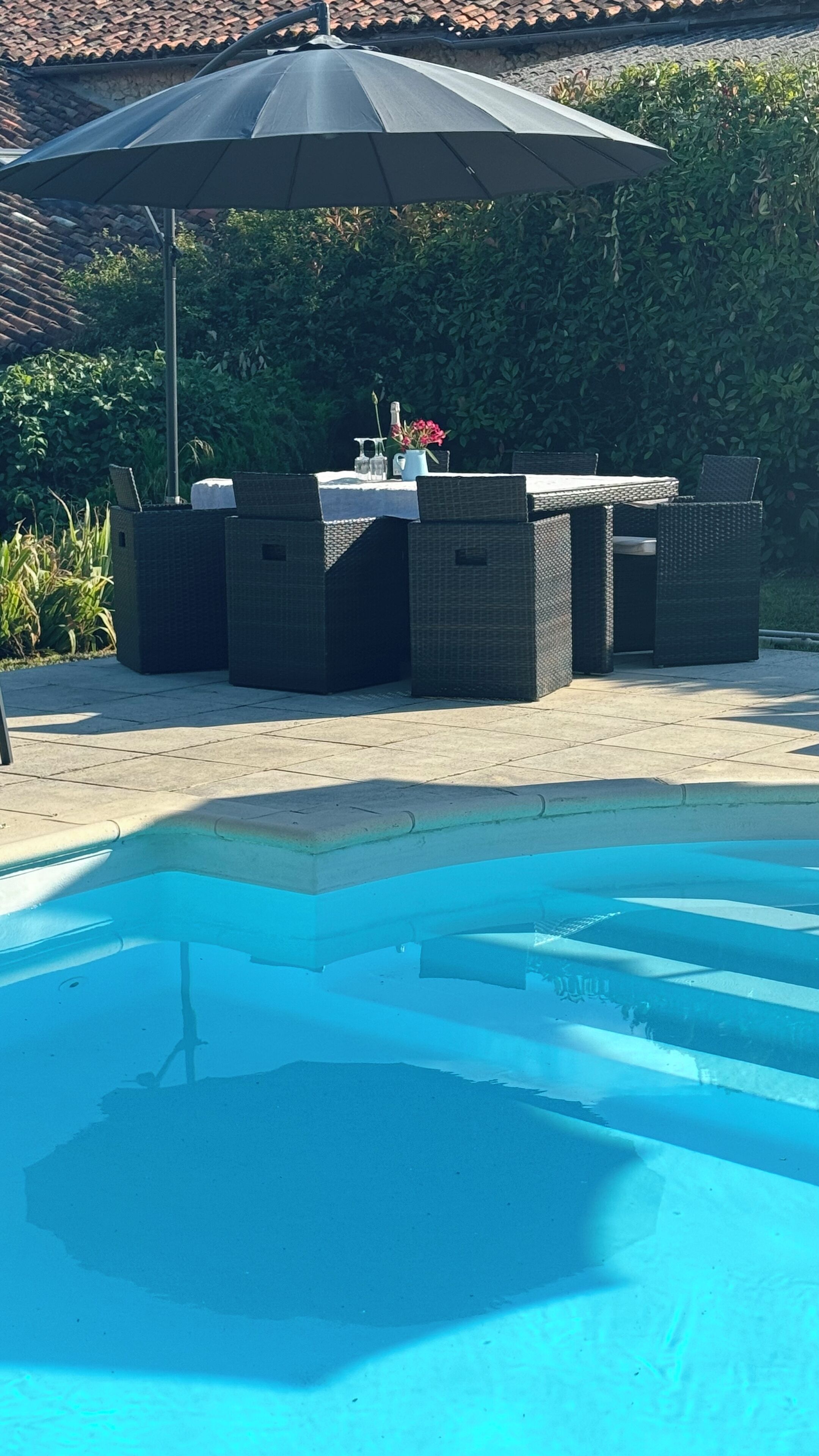 Ein Poolbereich im Freien mit Essbereich, der Korbmöbel und einen Tisch unter einem großen Sonnenschirm bietet.