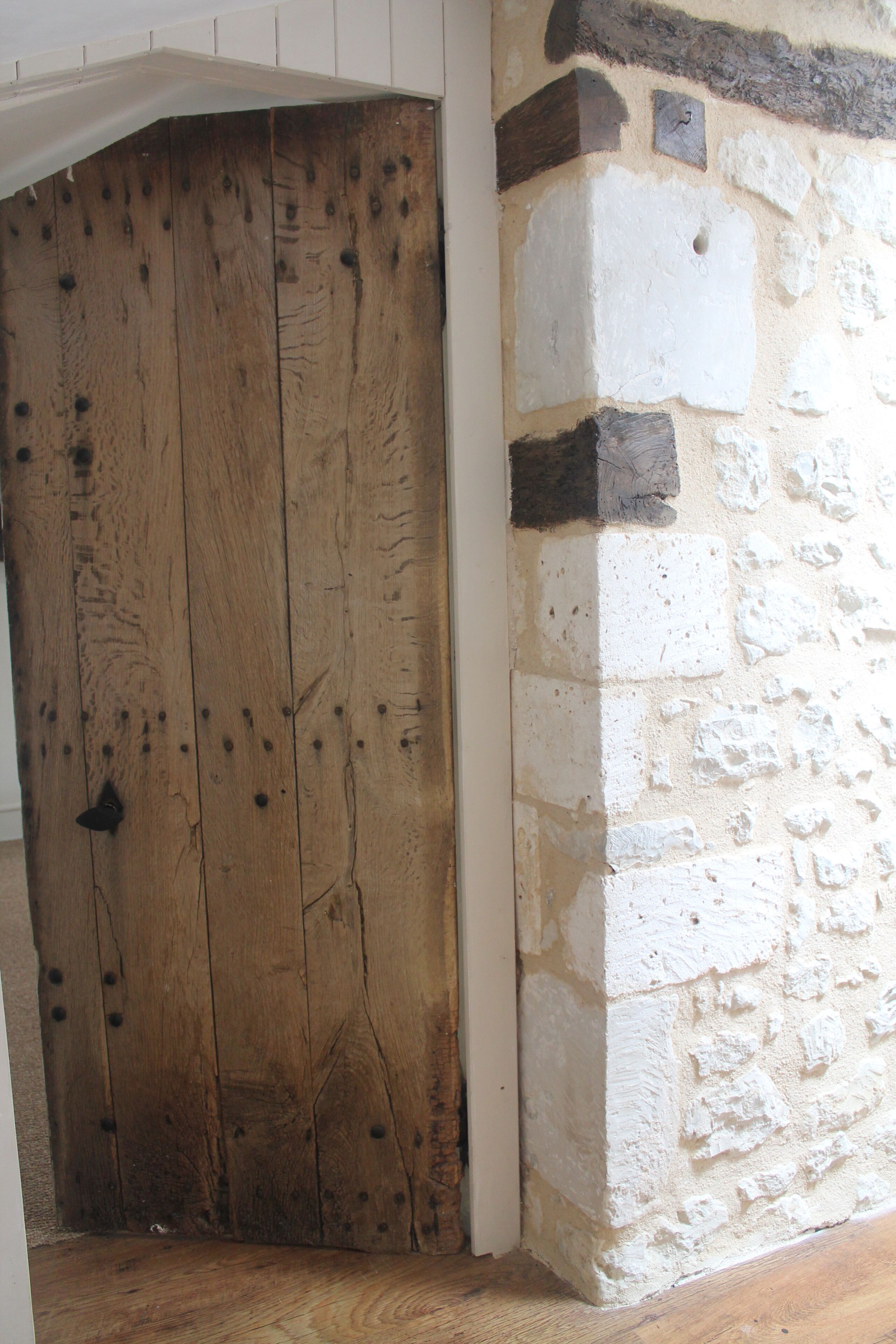 Una puerta de madera con vetas y nudos visibles, junto a una pared de piedra de textura rugosa y un pequeño agujero.