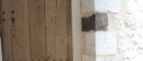 Una puerta de madera con vetas y nudos visibles, junto a una pared de piedra de textura rugosa y un pequeño agujero.