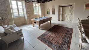 Une pièce avec une table de billard, un canapé, un tapis à motifs, des murs en pierre et des poutres en bois.