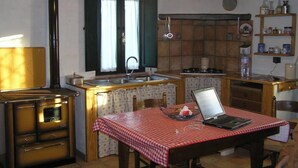 Una cocina pequeña con un lavamanos, estufa y una computadora portátil sobre una mesa.