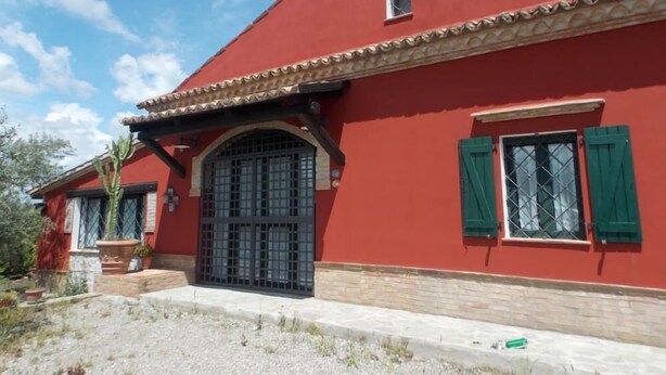Un edificio rojo con techo de tejas, un amplio ventanal de arco y contraventanas verdes.