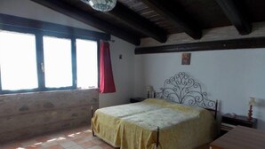 Un dormitorio con cama, mesita de noche, ventana con cortina roja y techo de madera.