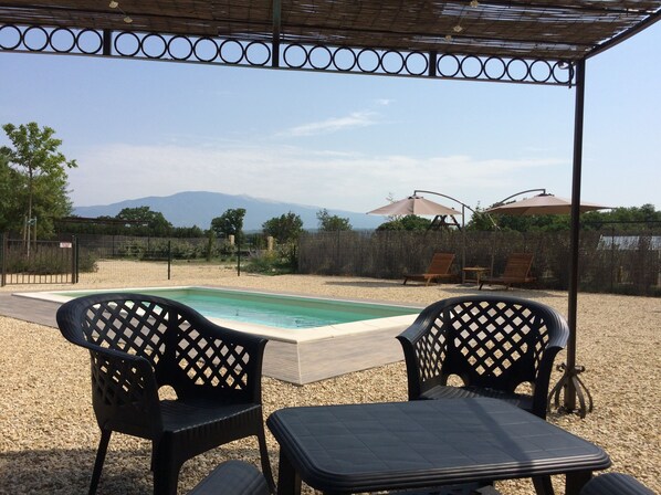 A pool area with two chairs and a table under a pergola, surrounded by a fence and a view of mountains. - Villa with private pool in the countryside near the village (Mazan)