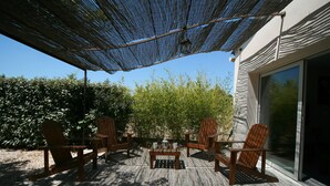 Una terrazza esterna con sedie e tavolo in legno, un pergolato che offre ombra e vista su un giardino e un edificio.