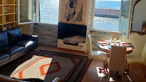 Sala de estar con un sofá de cuero negro, un tapiz estampado, una estantería y un amplio ventanal con vista al mar.