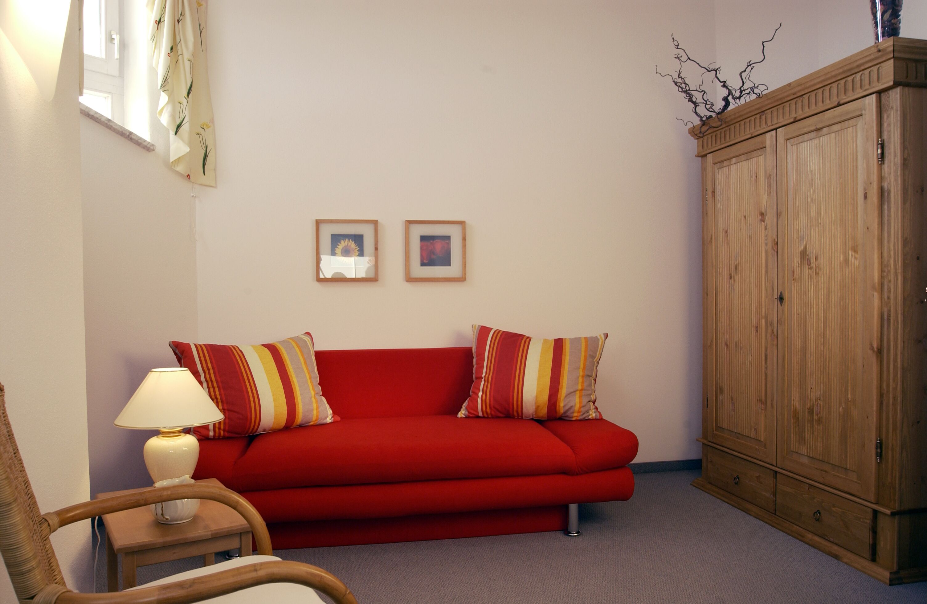 A living room with a red sofa, two pillows, a wooden cabinet, and a lamp on a side table.