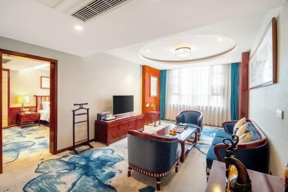A hotel room with a large window, a flat-screen TV, a sofa, a coffee table, and a desk with a chair.
