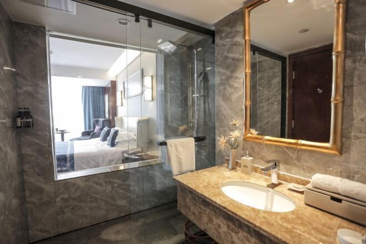 A modern bathroom with a large mirror, a marble sink, and a glass-enclosed shower.