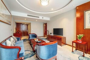 A modern living room with a sofa, chairs, a coffee table, a TV, and a small table with a plant. - Emeishan Yue Garden Hotel (Jiajiang)