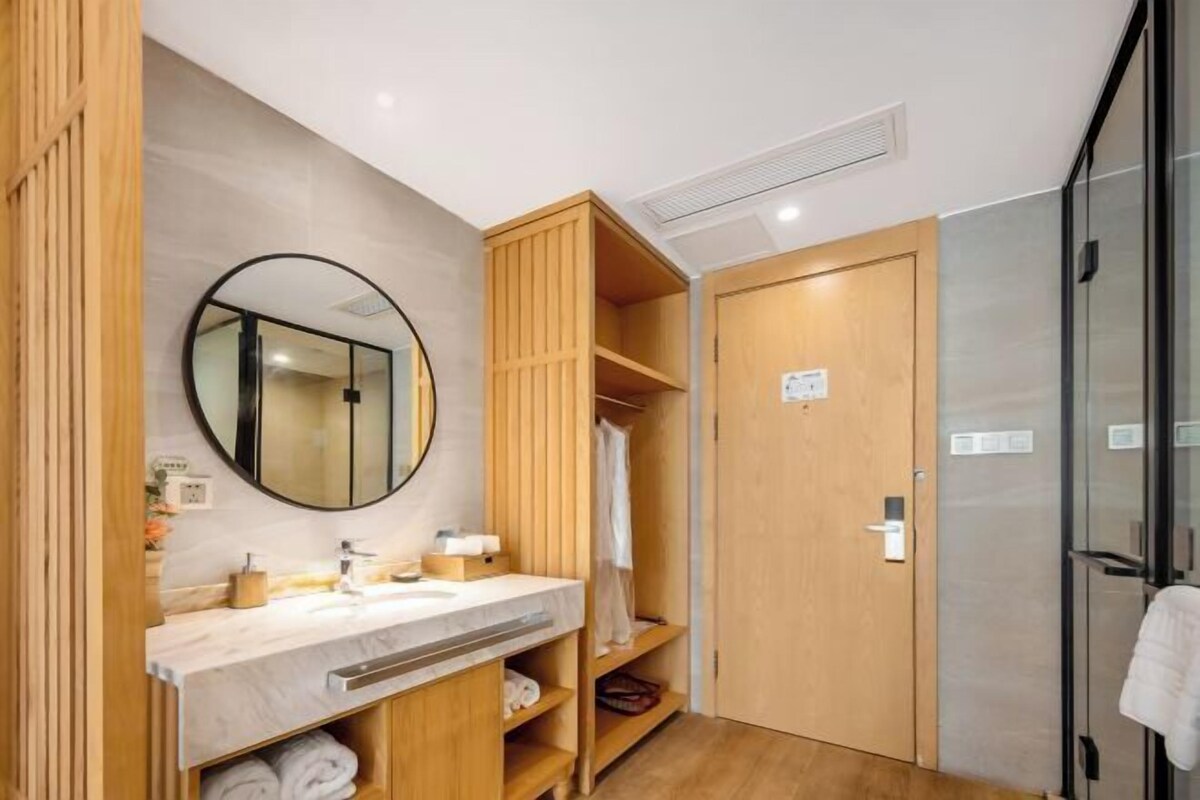 A modern bathroom with a vanity, mirror, wooden shelves, and a shower area.
