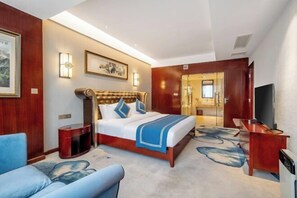 A hotel room with a large bed, a TV, a desk, and a bathroom visible through a glass door. - Emeishan Yue Garden Hotel (Jiajiang)