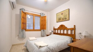 Une chambre à coucher avec un lit en bois, une table de chevet, un bureau, une fenêtre avec des rideaux et un tableau accroché au mur.