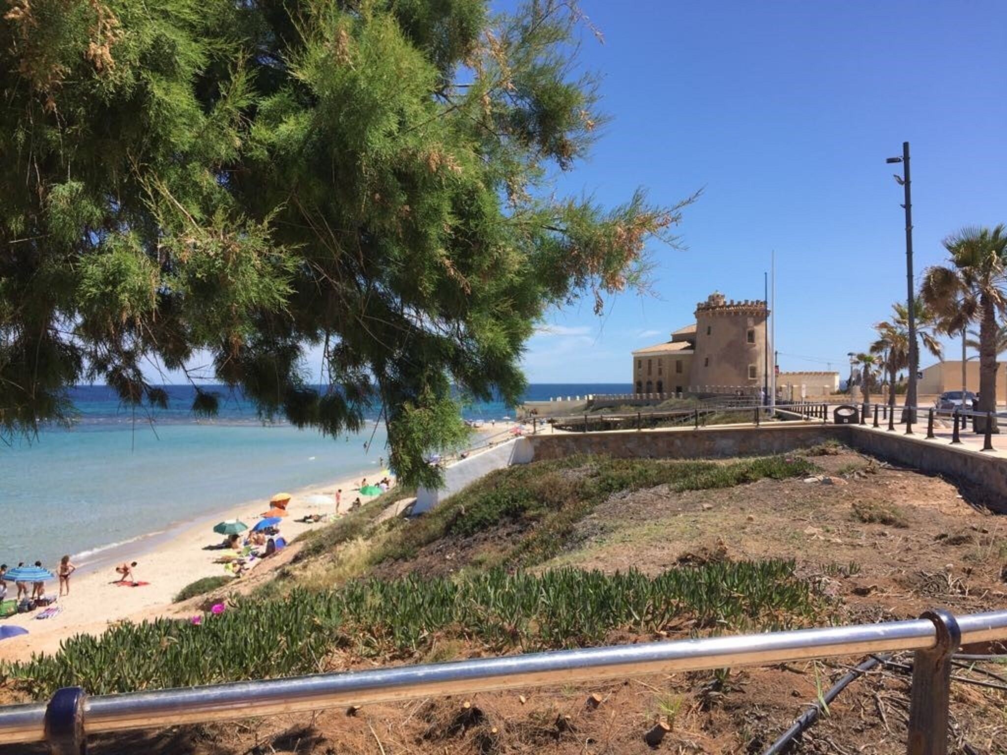 A coastal view with a beach, a castle-like building, and a clear sky.