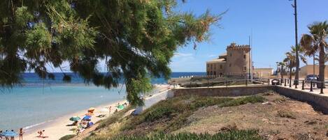 A coastal view with a beach, a castle-like building, and a clear sky.