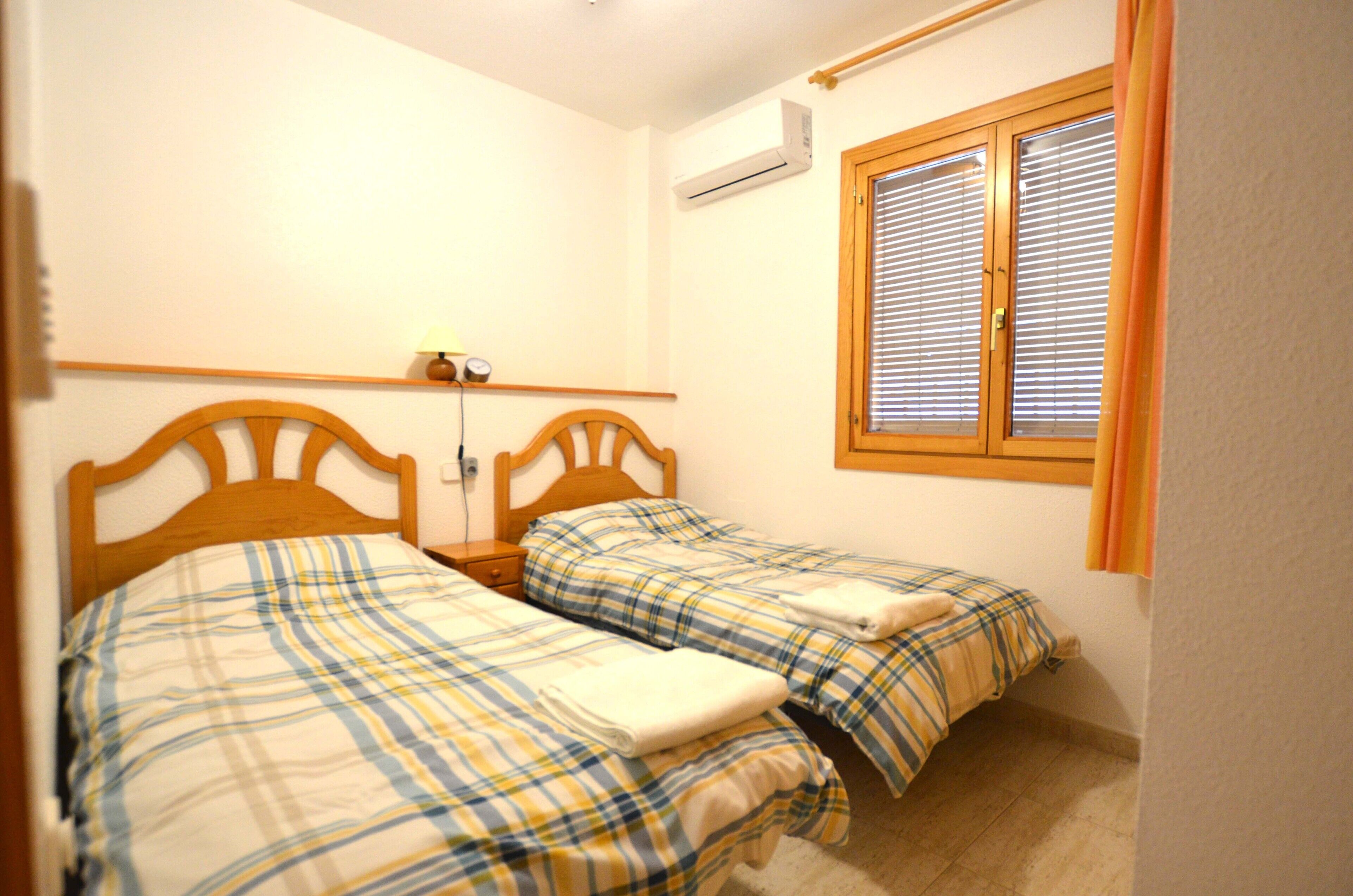 A bedroom with two beds, a nightstand, and a window with blinds.