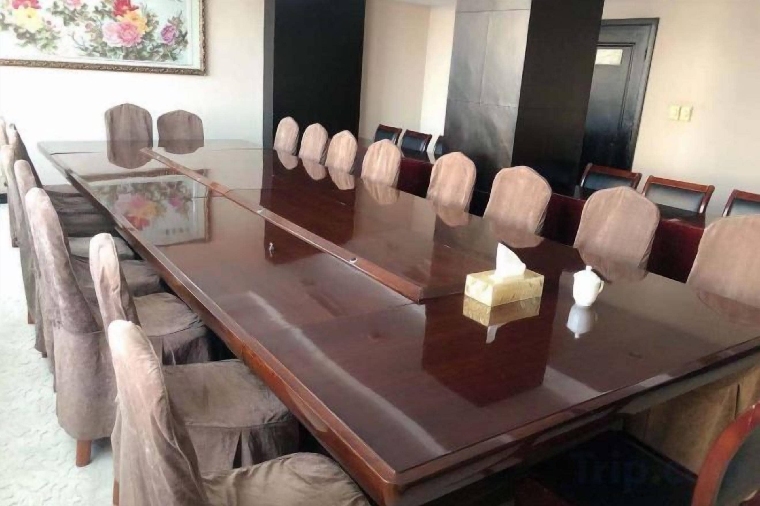 A conference room with a long wooden table, multiple chairs, and a small table with a tissue box.