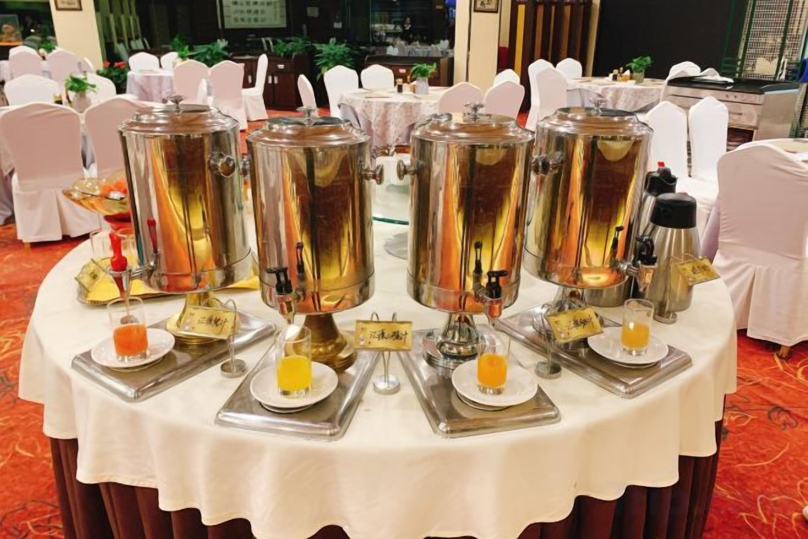 Montaje tipo bufé con múltiples dispensadores de acero inoxidable, cada uno con un nombre, y platos pequeños con bebidas anaranjadas.