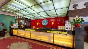 A hotel reception area with a glass ceiling, a red wall with a decorative plate, and a reception desk with a red lamp.