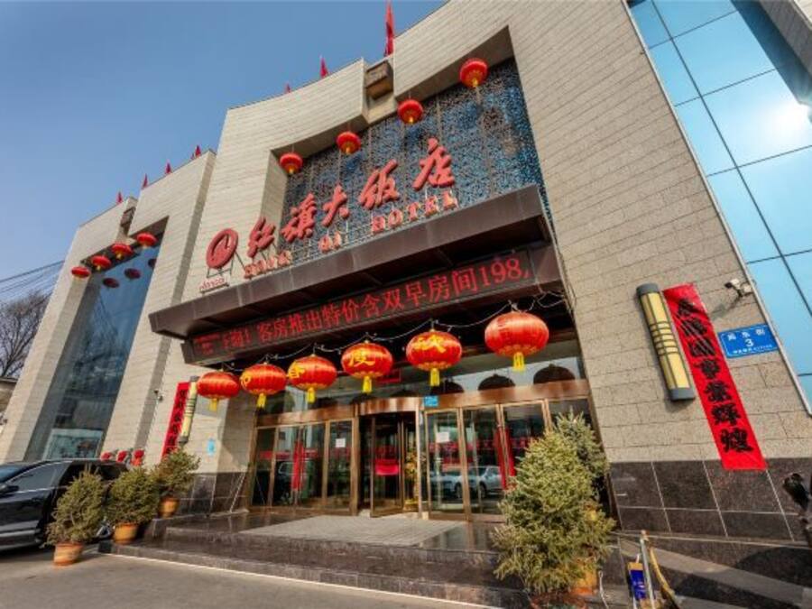 A hotel entrance with a large sign, red lanterns, and potted plants.