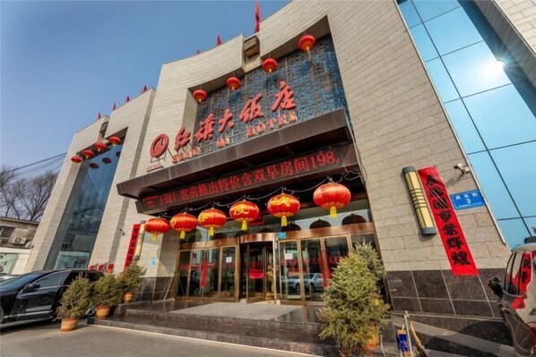 A hotel entrance with a large sign, red lanterns, and potted plants.