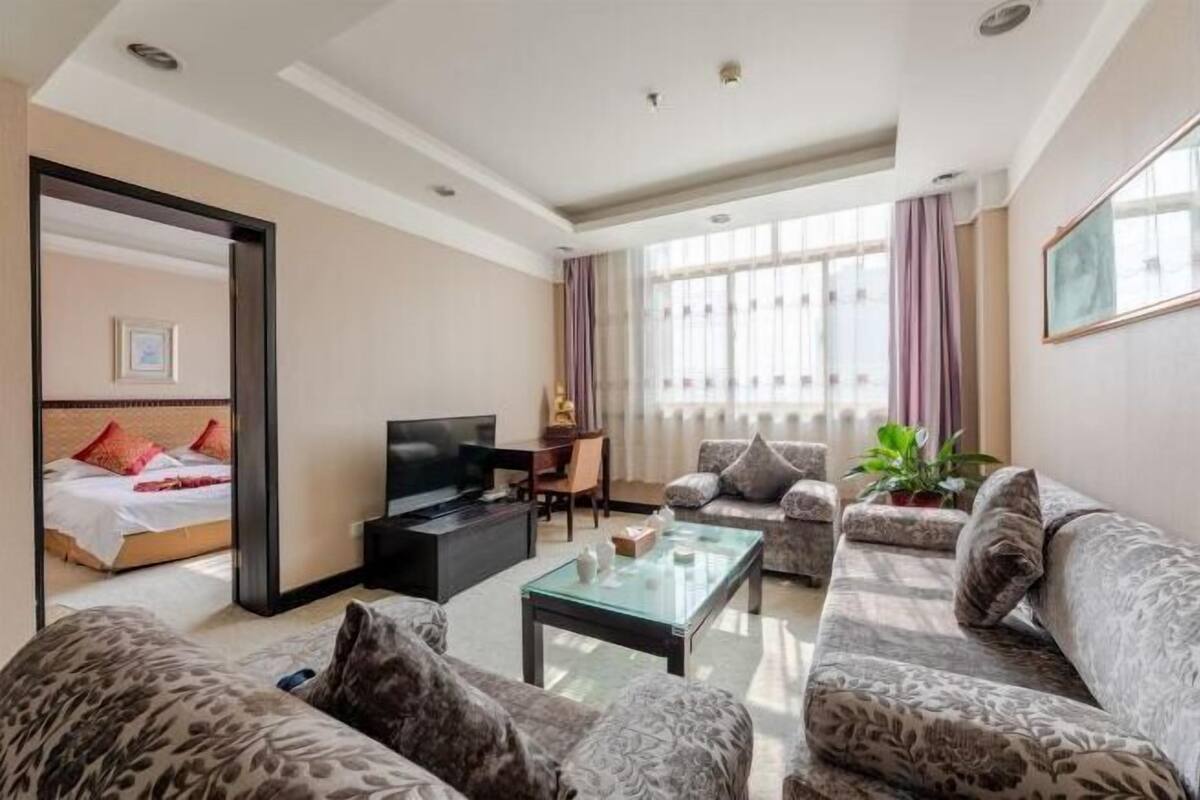A modern hotel room with a large bed, a flat-screen TV, a sofa, a coffee table, and a large mirror.