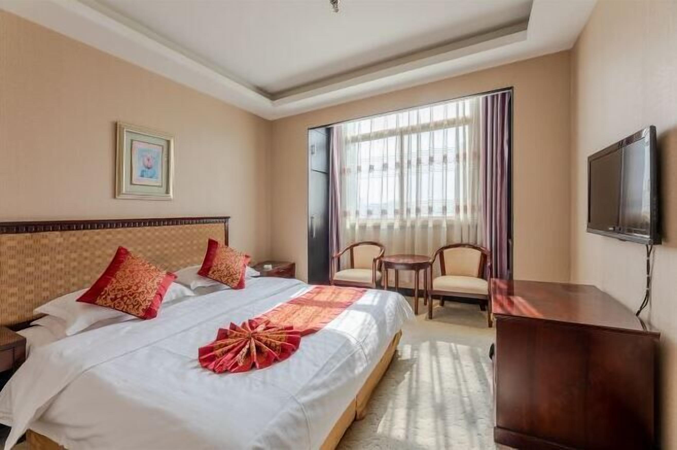 A hotel room with a large bed, a desk, a chair, a TV, and a window with curtains.