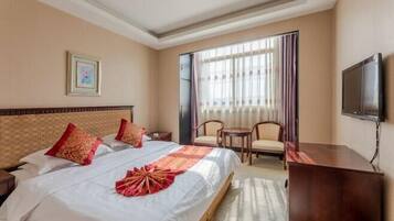A hotel room with a large bed, a desk, a chair, a TV, and a window with curtains.