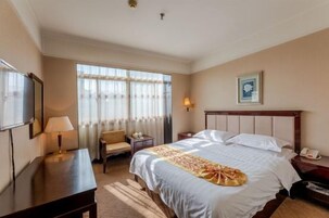Habitación de hotel con cama, escritorio, silla, lámpara, mesita de noche y ventana con cortinas.
