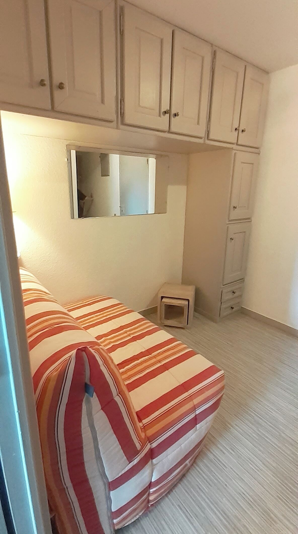 Quarto com cama, um banquinho e um guarda-roupa.