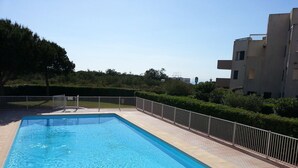 En rektangulär swimmingpool med ett kaklat poolområde, omgiven av ett staket av metall och häckar.