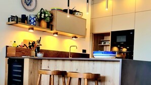 Eine moderne Küche mit Holzbarhocker, Pendelleuchten und einem eingebauten Backofen.