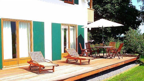 A wooden deck with lounge chairs and a table, adjacent to a building with green shutters and a white facade. - Sunny, spacious & fully equipped, castle views, close to lake/beach, restaurants (Schwangau)