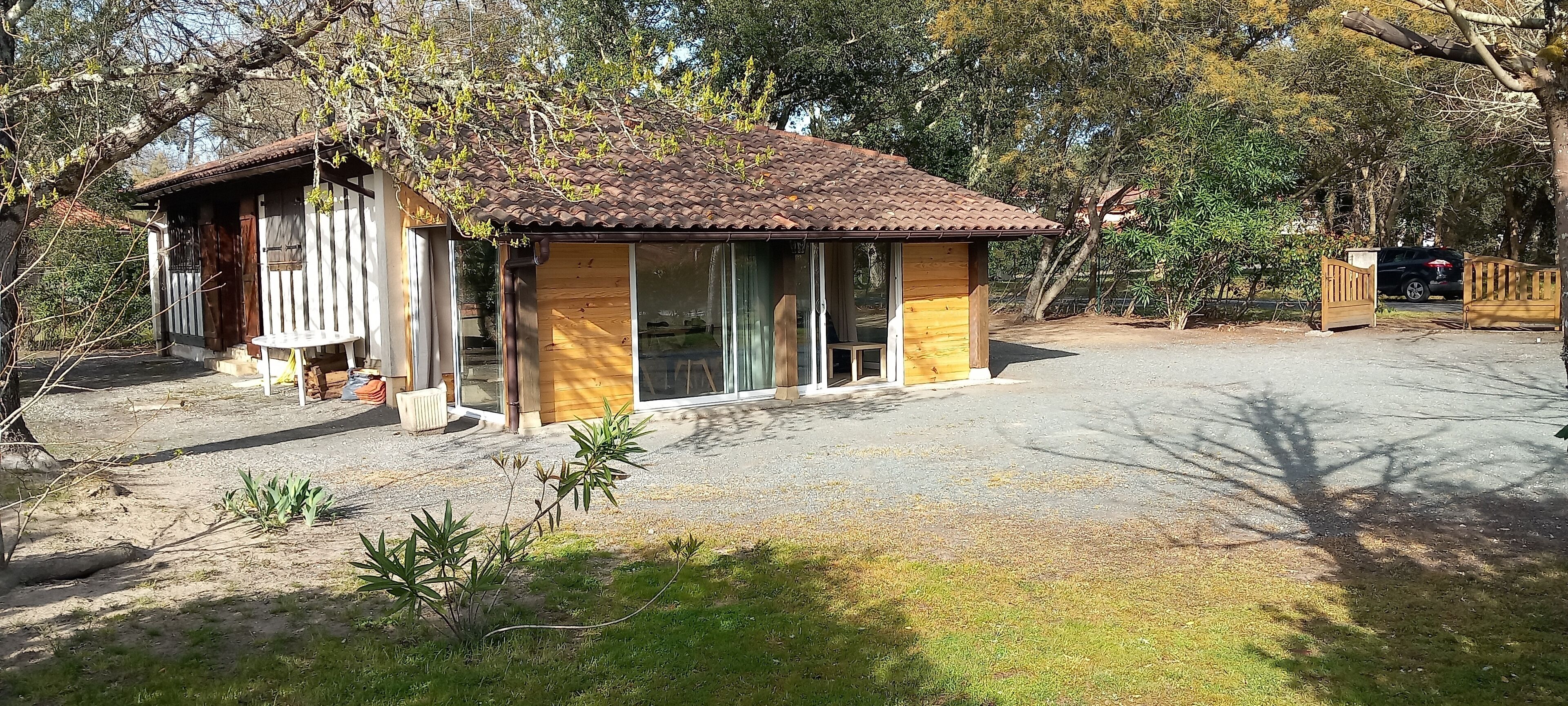 A small wooden house with a tiled roof, a covered porch, and a gravel driveway.