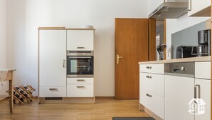 A modern kitchen with white cabinetry, a built-in oven, a coffee maker, and a wine rack. - Spacious vacation home with Moselle view, 8 pers., 3 bathrooms, free of charge. Public transport ticket (Ürzig)