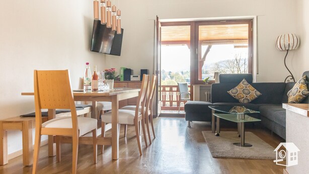A modern living room with a dining area, a sofa, and a TV mounted on the wall. - Spacious vacation home with Moselle view, 8 pers., 3 bathrooms, free of charge. Public transport ticket (Ürzig)