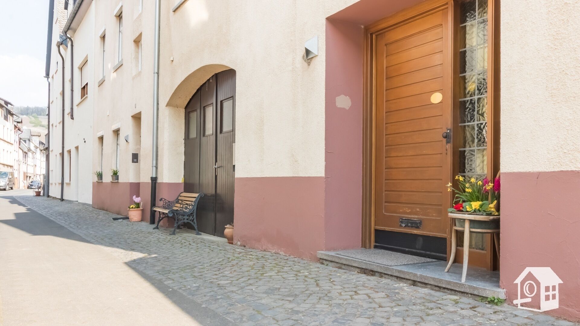 Un bâtiment situé sur une rue pavée, avec une porte en bois et un banc à l’extérieur.