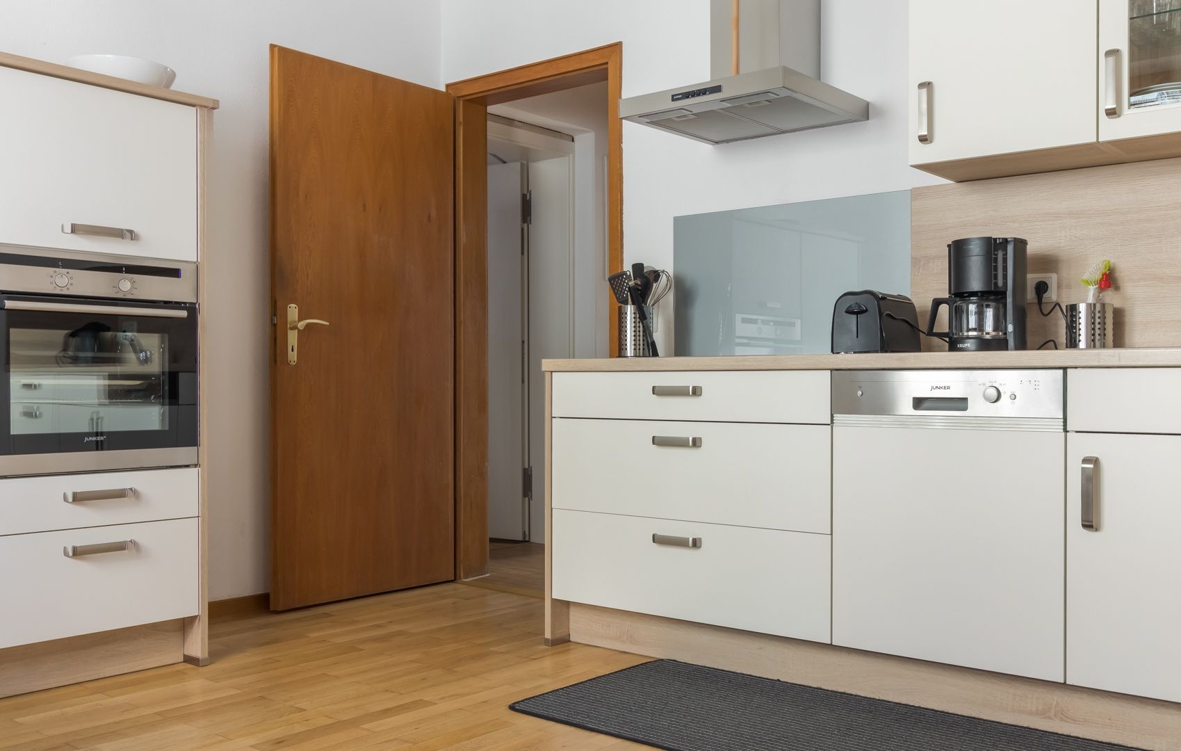Ett modernt kök med vita skåp, en inbyggd ugn, en kaffebryggare och en diskmaskin.