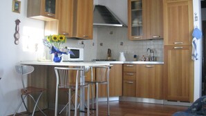 A kitchen with wooden cabinets, a microwave, a sink, and a vase with flowers on the counter. - Formosa Apartment: A Wonderful Holiday in the Heart of Gorgeous Venice (Venezia)