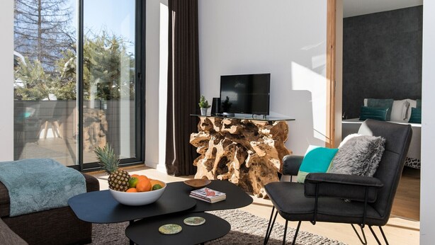 Un salon moderne doté d’une grande fenêtre, d’un téléviseur à écran plat, d’une table basse en bois et d’un coin salon confortable.