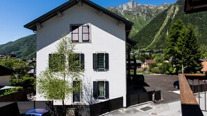 Un immeuble blanc à deux étages, doté de volets noirs, d’un balcon et offrant une vue sur une chaîne de montagnes.